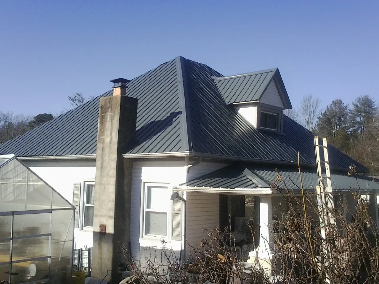 Dark blue standing seam metal roof on a white farmhouse with dormer — Slate & Tile Roof Repair by Roofing Brothers in Browntown