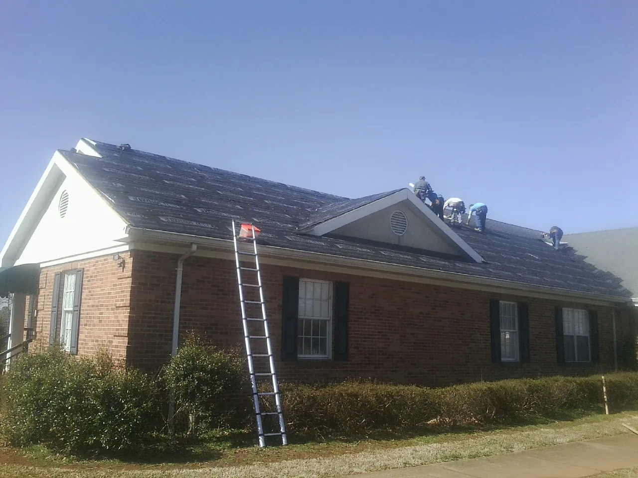 Crew tearing shingles off a brick ranch roof with a ladder set — Emergency Roof Repair work by our crew in Browntown