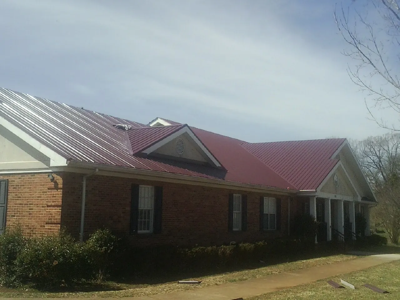 Red metal roof with gabled entries on a long brick building, from a Hail Damage Roof Repair job in Browntown