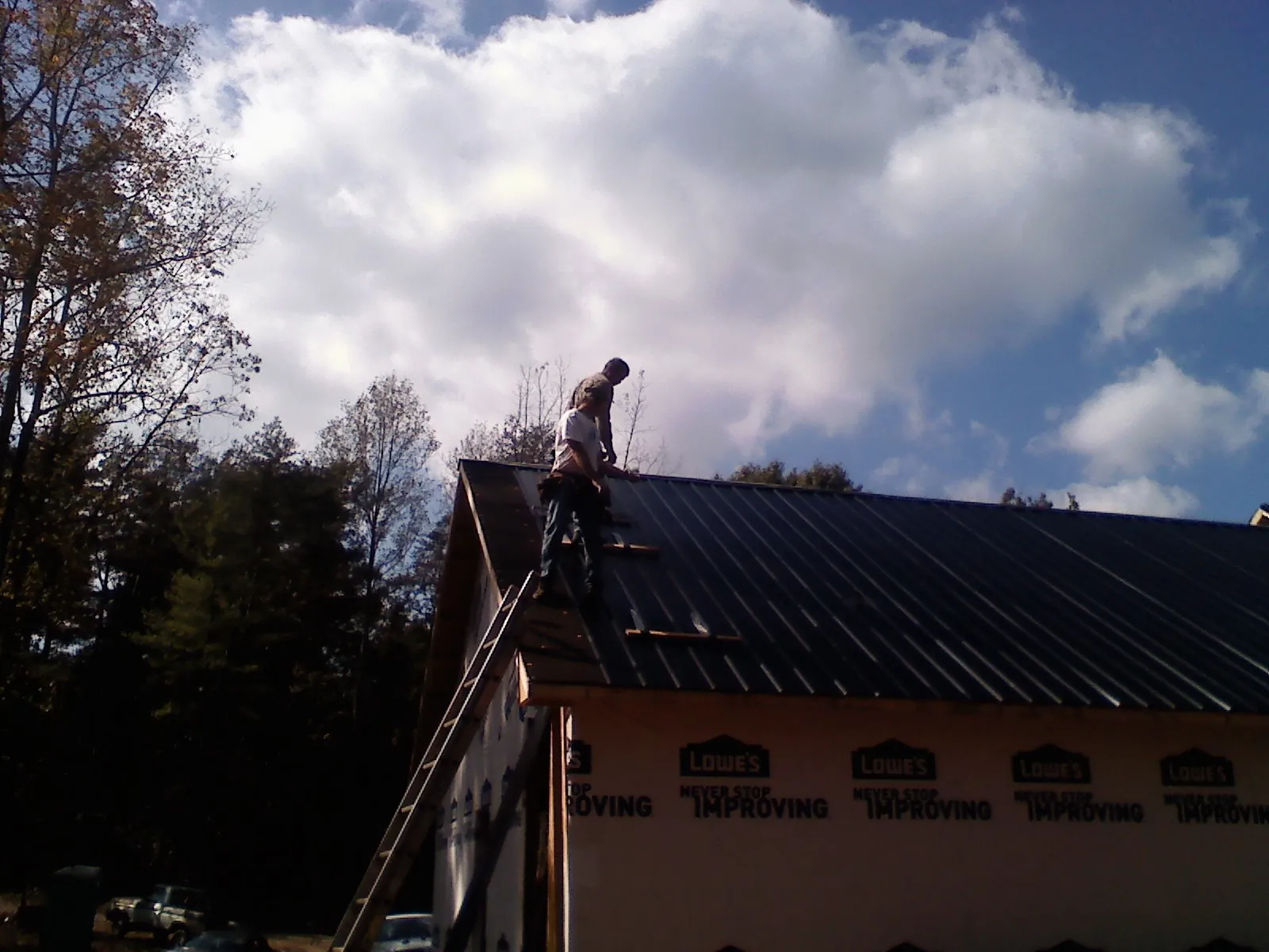 Roofer fastening dark metal panels high against a cloudy sky, from a Roof Inspection job in Browntown