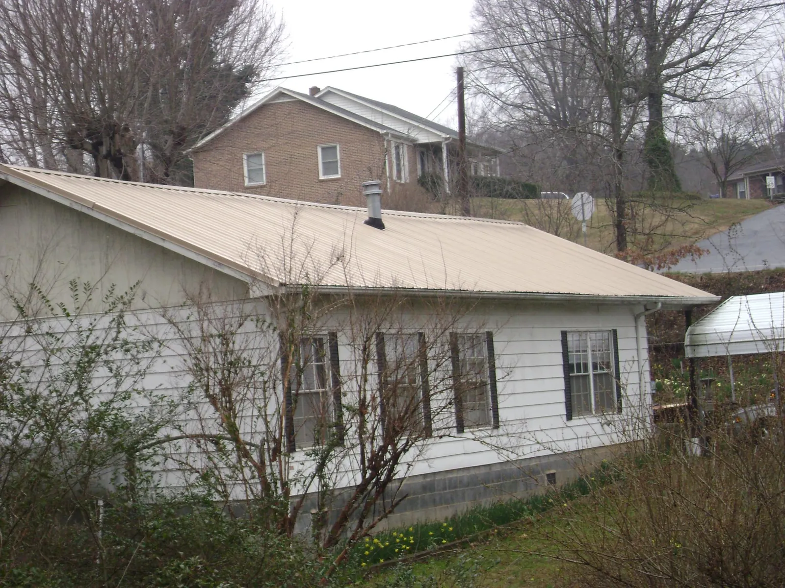 Tan metal roof on a white sided house set into a hillside — Commercial Roofing by Roofing Brothers in Browntown